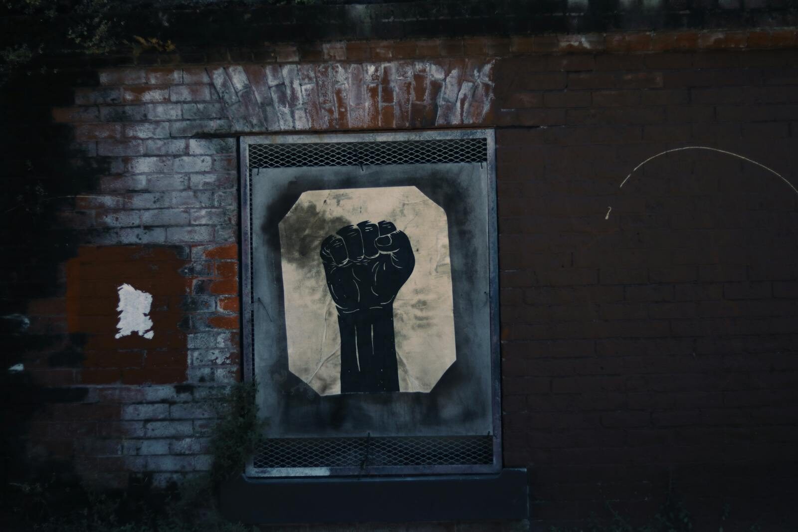 Powerful street art featuring a black fist painted on a weathered brick wall.